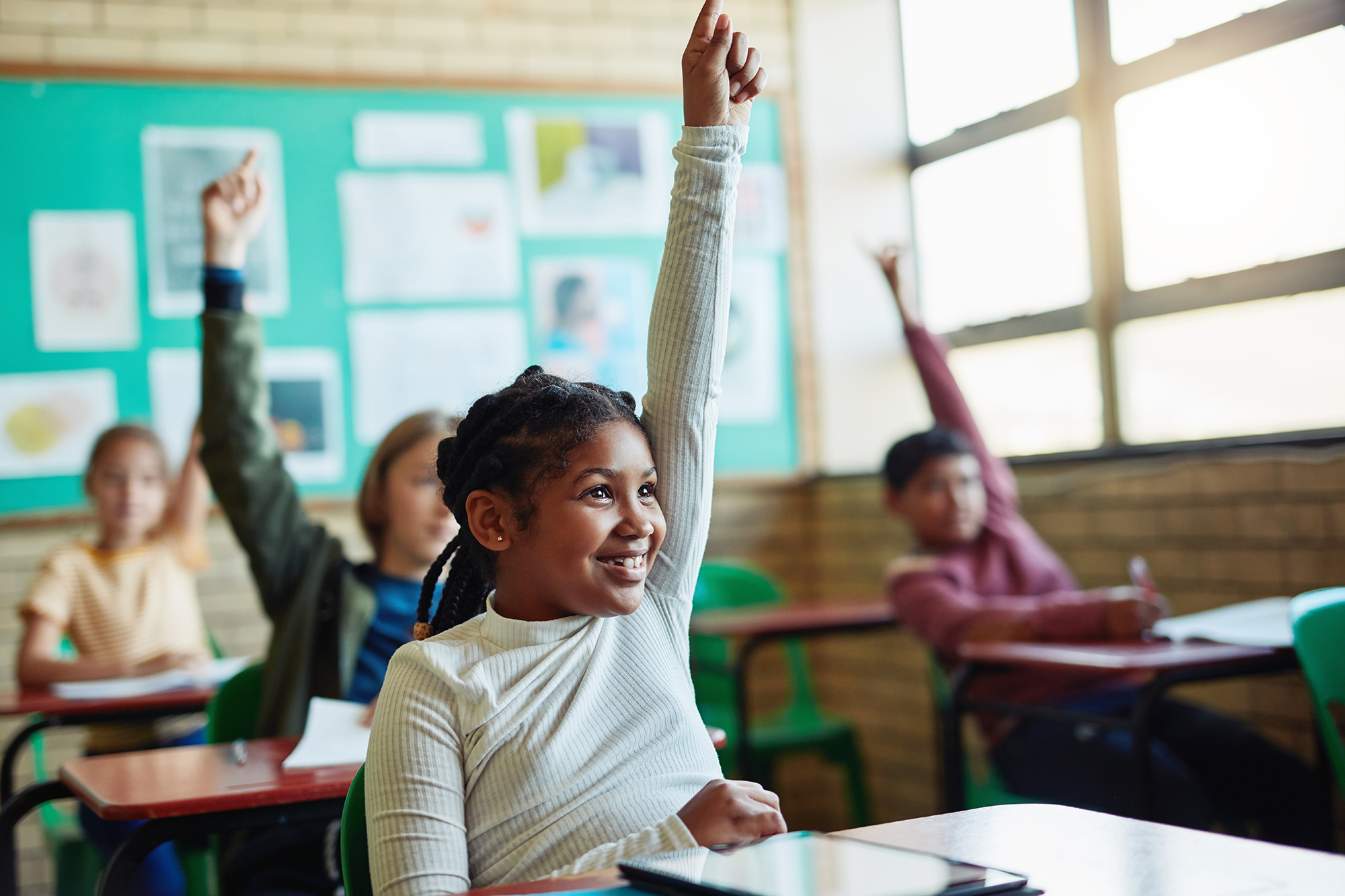 Photo of young children raising their hands in a classroom